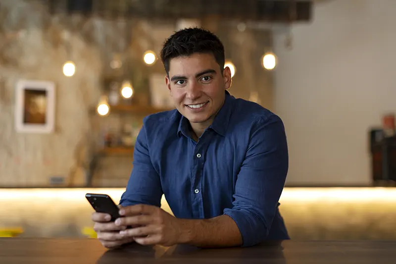 Hombre sonriente usando su celular en un espacio interior